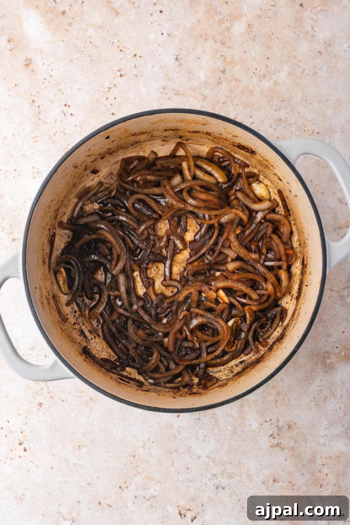 Sautéed onions in a Dutch Oven, browned and caramelized, on a speckled countertop.