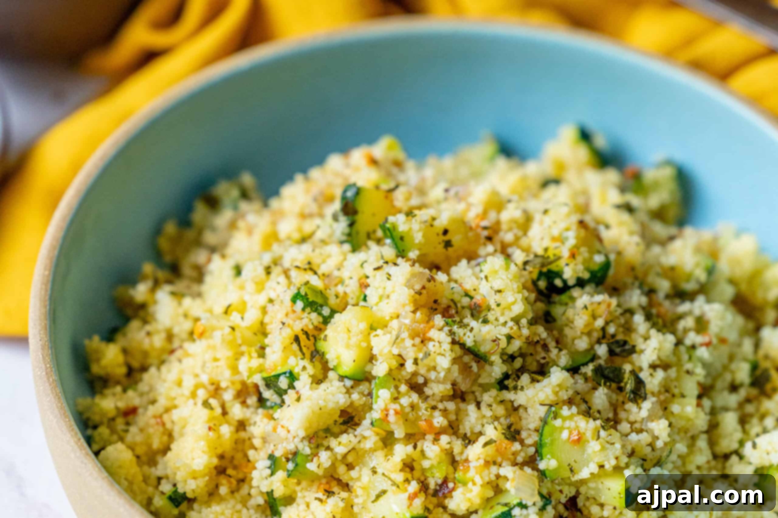 Zucchini Couscous Salad 8 A bowl of couscous mixed with diced vegetables and herbs, beautifully presented against a blurred yellow fabric background, highlighting its fresh and inviting appearance.