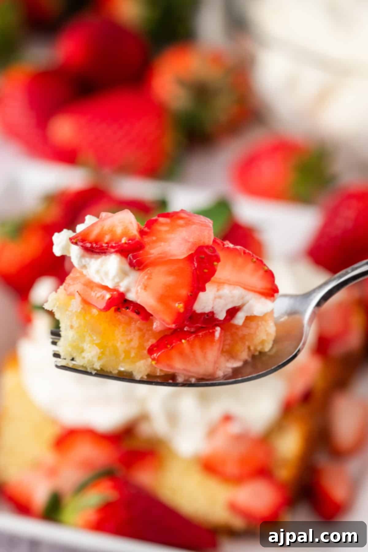 Summer Berry Shortcake 12 A slice of strawberry shortcake adorned with juicy strawberries, whipped cream, and a mint garnish rests on a white plate. A fork is cutting into the dessert. Fresh strawberries and a bowl of cream enhance the background's allure.