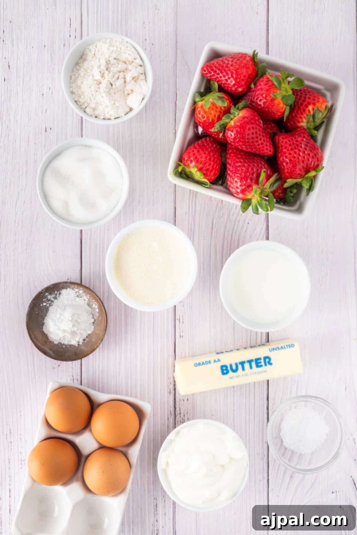 Summer Berry Shortcake 5 A delightful scene on a light wooden surface unveils the key ingredients for a strawberry shortcake: fresh strawberries, butter, flour, sugar, eggs, cream, yogurt, baking powder, and salt.