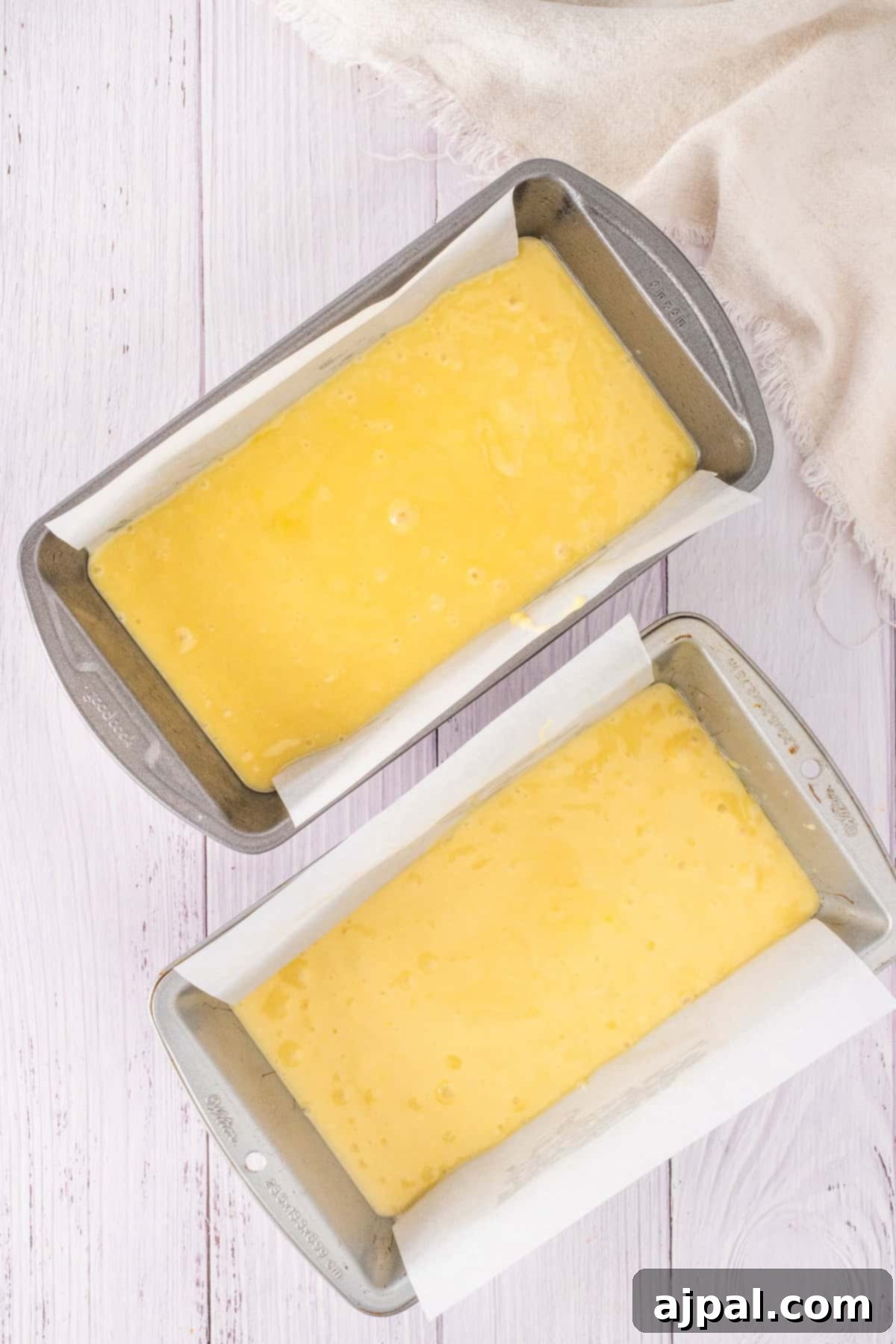 Summer Berry Shortcake 7 A bowl of yellow cake batter with a whisk attachment sits on a light wooden surface, hinting at the creation of a delightful strawberry shortcake. Nearby, a cloth rests casually, ready to assist in crafting this sweet treat.