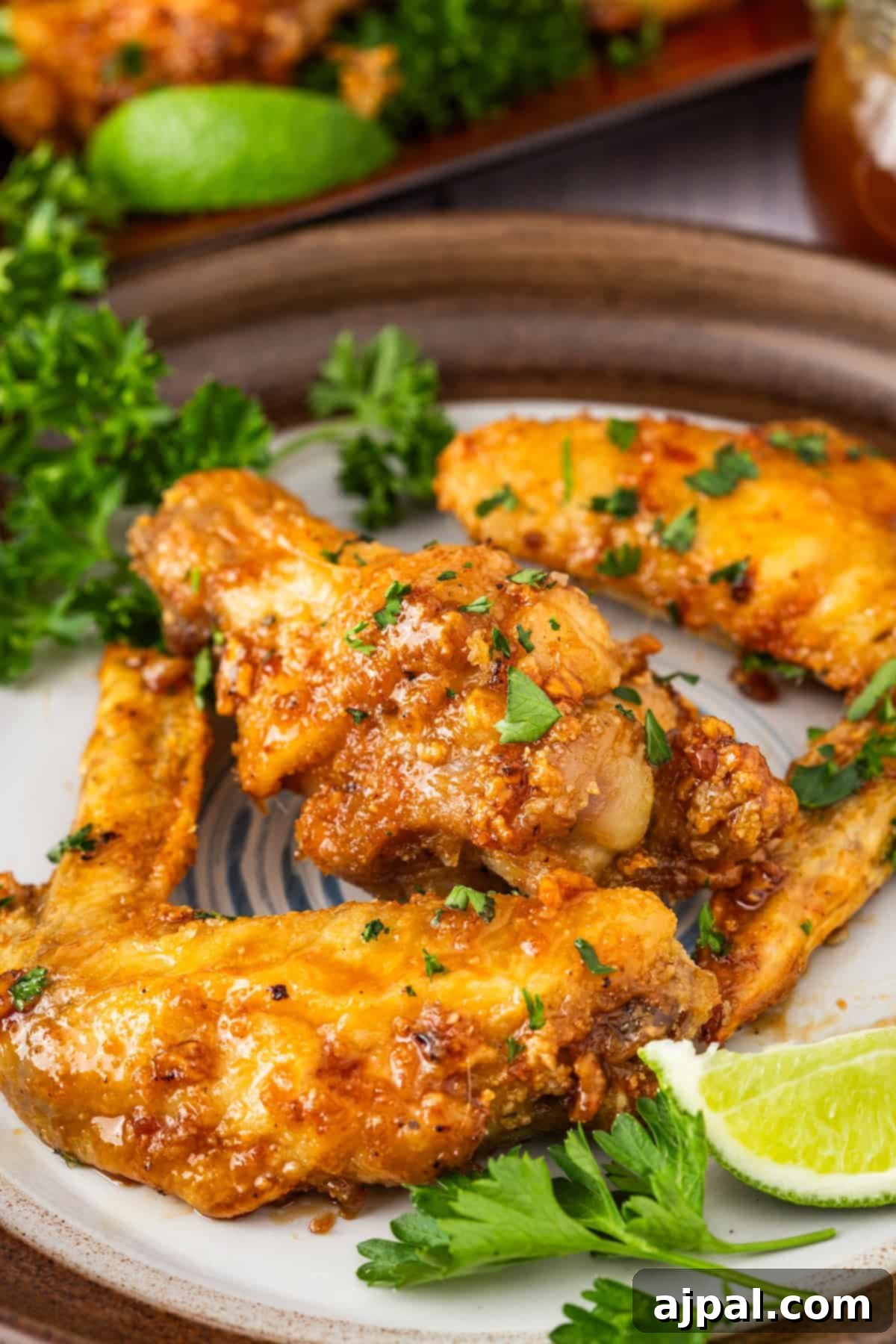 A close-up of honey garlic wings, crispy and adorned with parsley. A lime wedge and fresh parsley sit invitingly on the side.