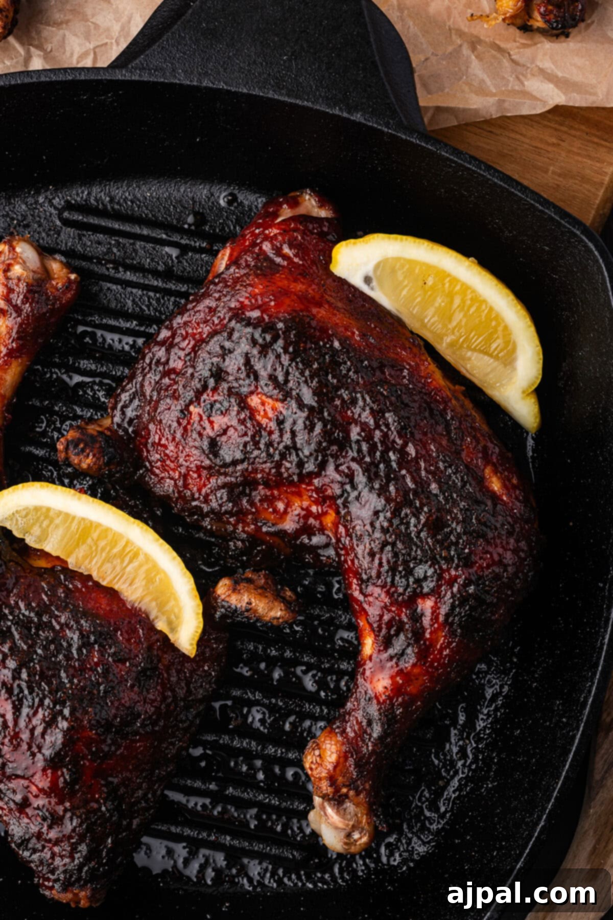 Juicy BBQ Chicken Quarters 3 Grilled chicken quarters with a rich, BBQ-glazed coating sizzle in a cast-iron pan, garnished with lemon wedges.