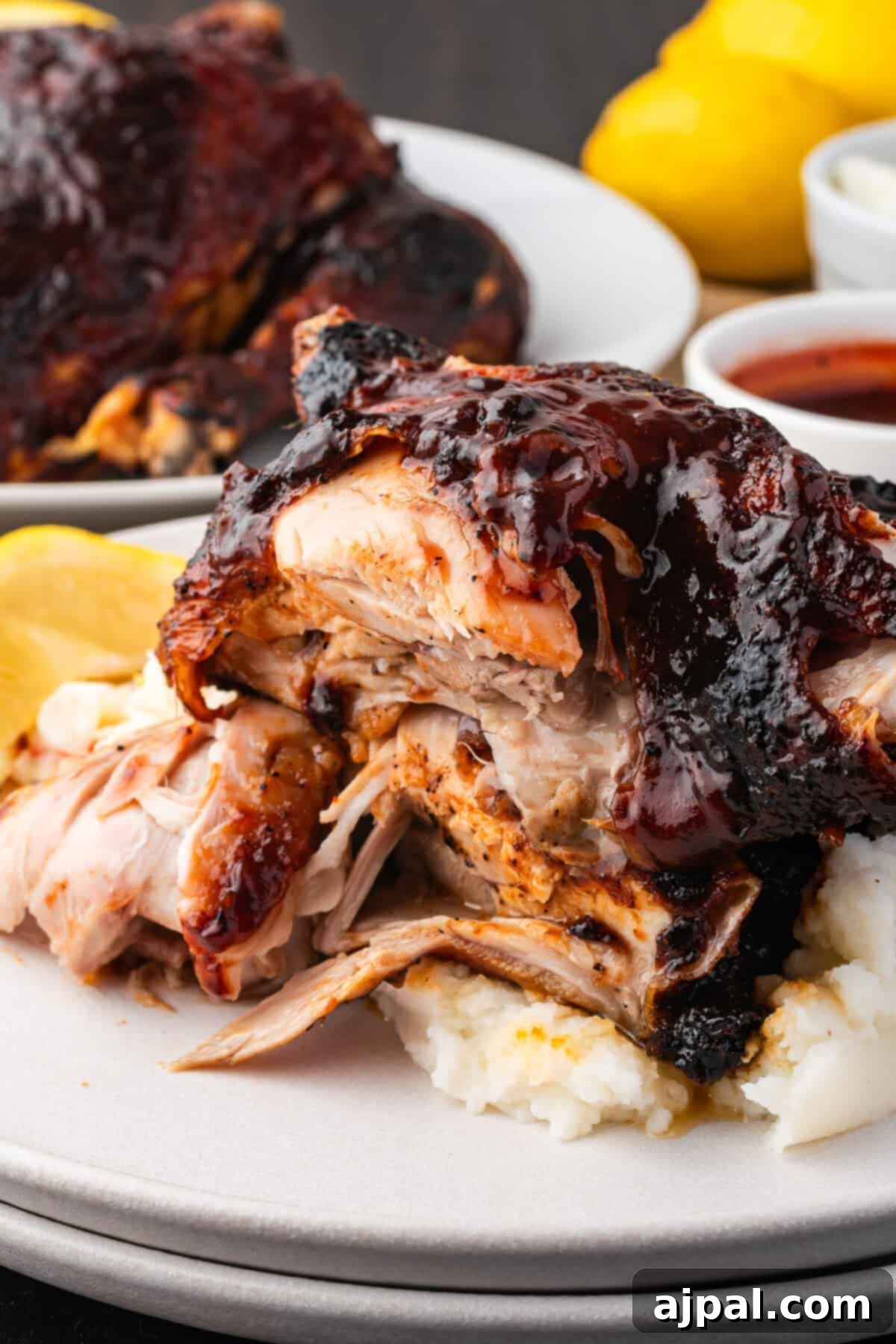 Juicy BBQ Chicken Quarters 4 A plate of BBQ chicken quarters with a dark glaze rests on a bed of mashed potatoes, garnished with lemon slices. Lemon and barbecue sauce are in the background.