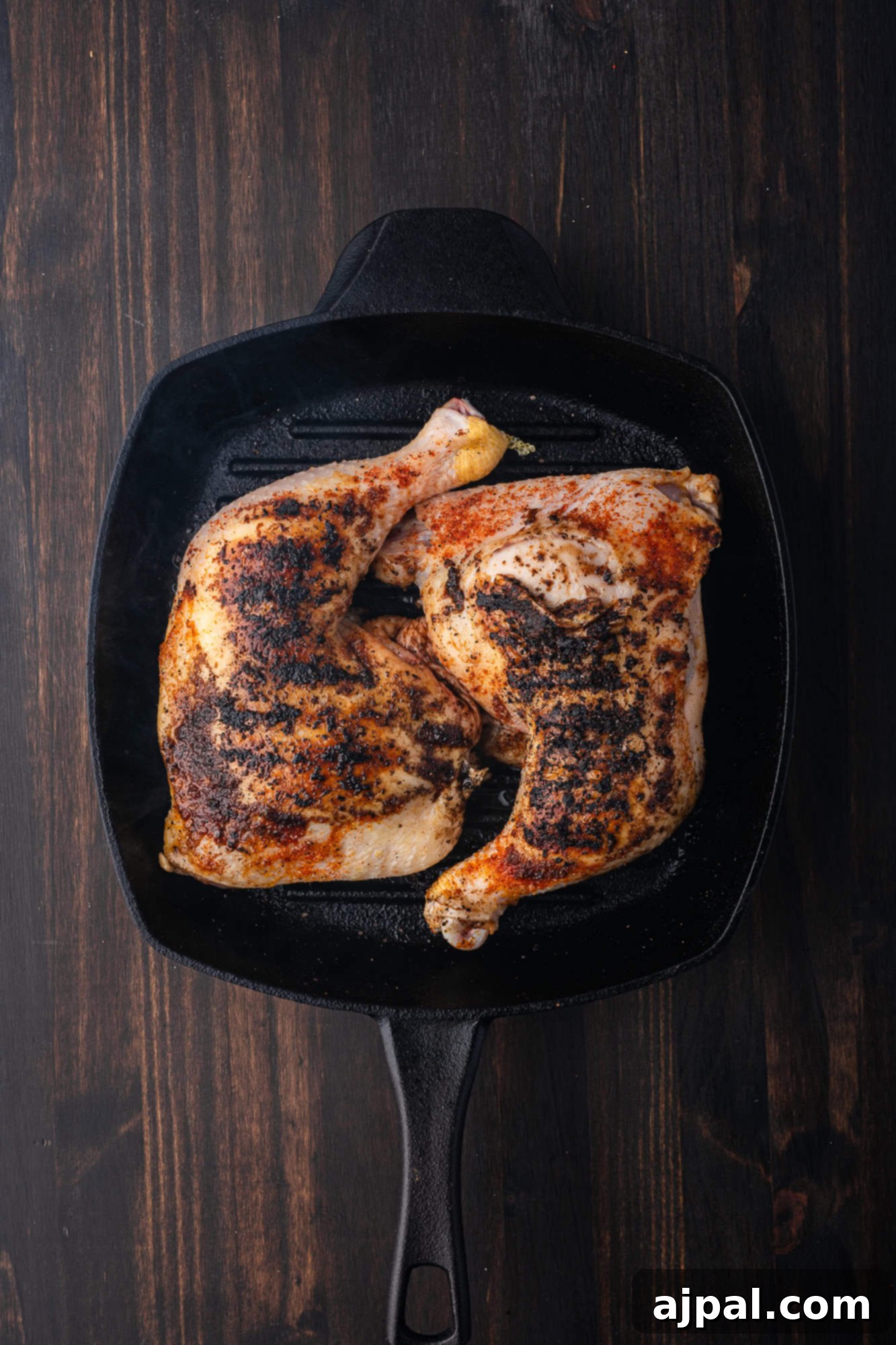 Juicy BBQ Chicken Quarters 8 Two BBQ chicken quarters with crispy skin and seasoning rest in a black cast iron skillet on a dark wooden surface.