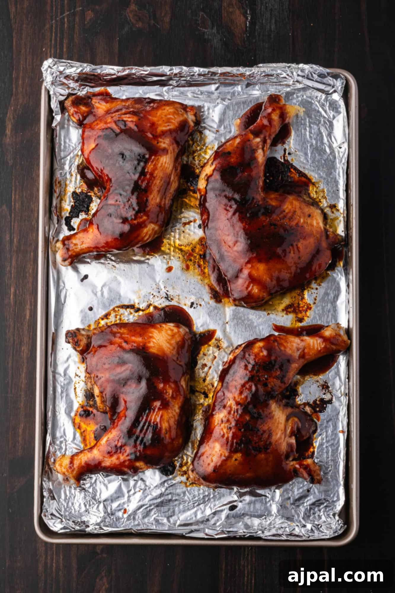 Juicy BBQ Chicken Quarters 10 Four BBQ chicken legs with crispy skin and dark glaze rest on a foil-lined baking sheet, perfecting an easy BBQ recipe.