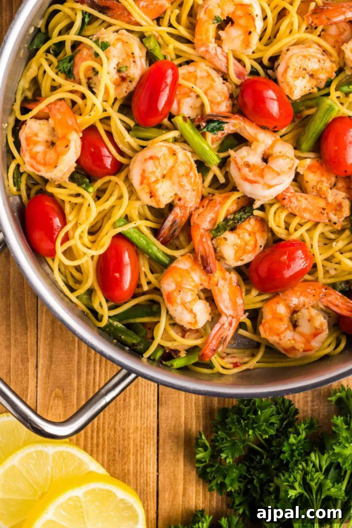 Lemon Garlic Shrimp Pasta 2 A skillet brimming with garlic-infused pasta, featuring succulent shrimp, cherry tomatoes, and tender asparagus. Lemon slices and parsley are placed nearby to enhance the fresh flavors.