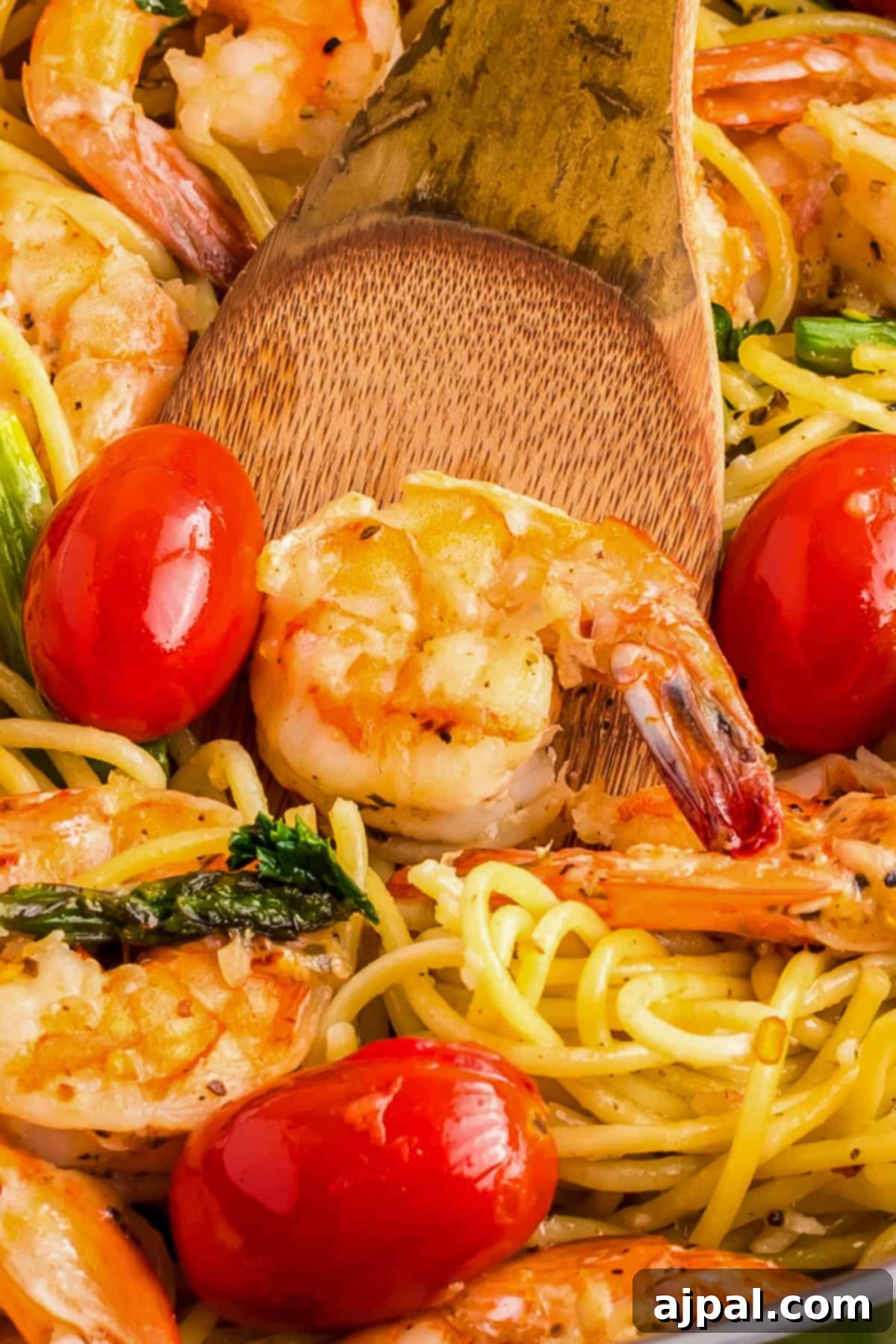 Lemon Garlic Shrimp Pasta 3 Close-up of pasta tossed with succulent shrimp, garlic, and cherry tomatoes, all mixed with spaghetti and fresh herbs, stirred with a wooden spoon.