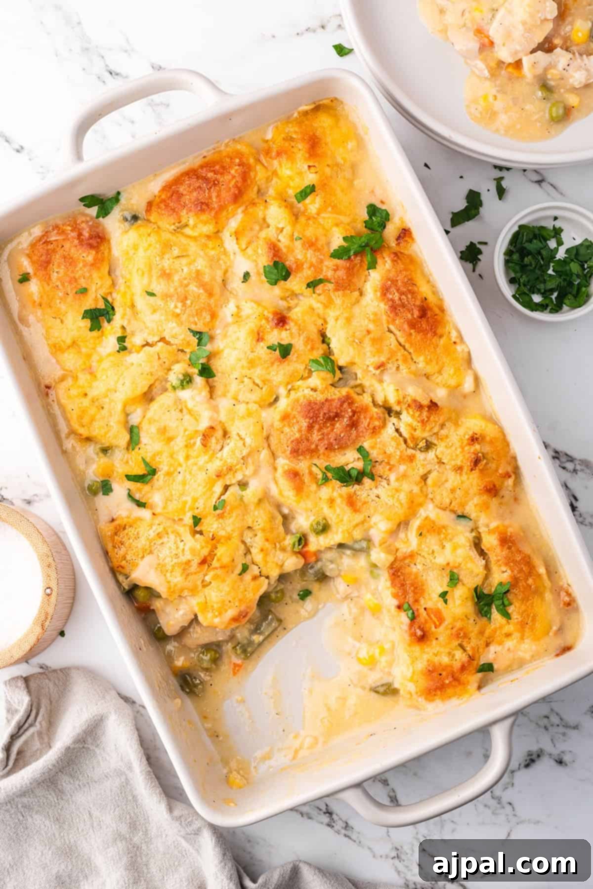 Comforting Chicken and Dumpling Bake 12 A Chicken Dumpling Casserole featuring a golden, biscuit-like topping and creamy filling, garnished with chopped parsley in a white rectangular dish.