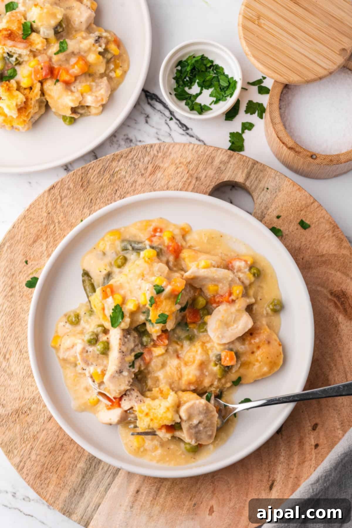 Comforting Chicken and Dumpling Bake 16 A plate of creamy chicken pot pie with vegetables, served on a wooden board. This delightful casserole includes tender chicken, offering cozy comfort on every bite. A small bowl of parsley and a wooden container sit nearby, enhancing the rustic charm.