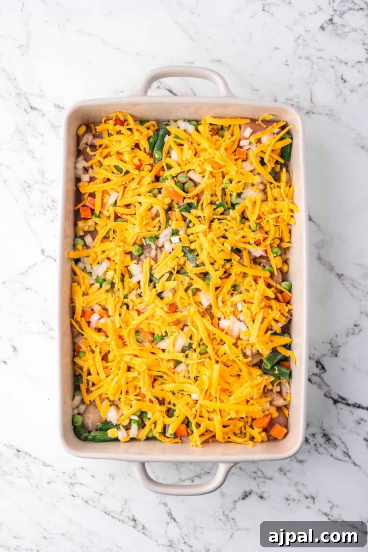 Comforting Chicken and Dumpling Bake 6 A rectangular baking dish filled with mixed vegetables, shredded cheese, and tender chicken rests on a marble countertop, resembling a delightful casserole.