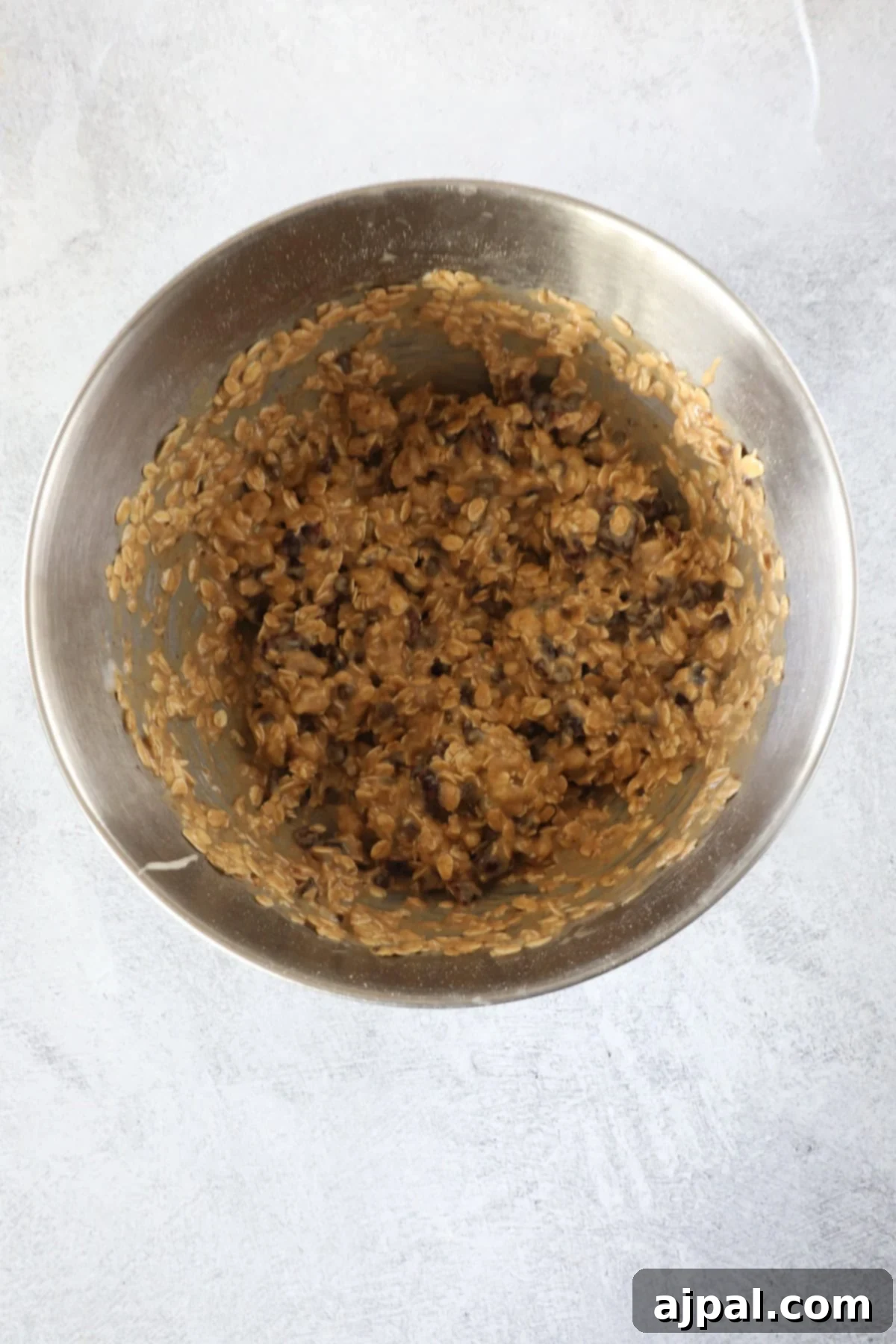 Artisan Sourdough Granola Bites 5 A metal mixing bowl filled with a mixture of oats, chocolate chips, and batter for sourdough granola bars sits on a light gray countertop.