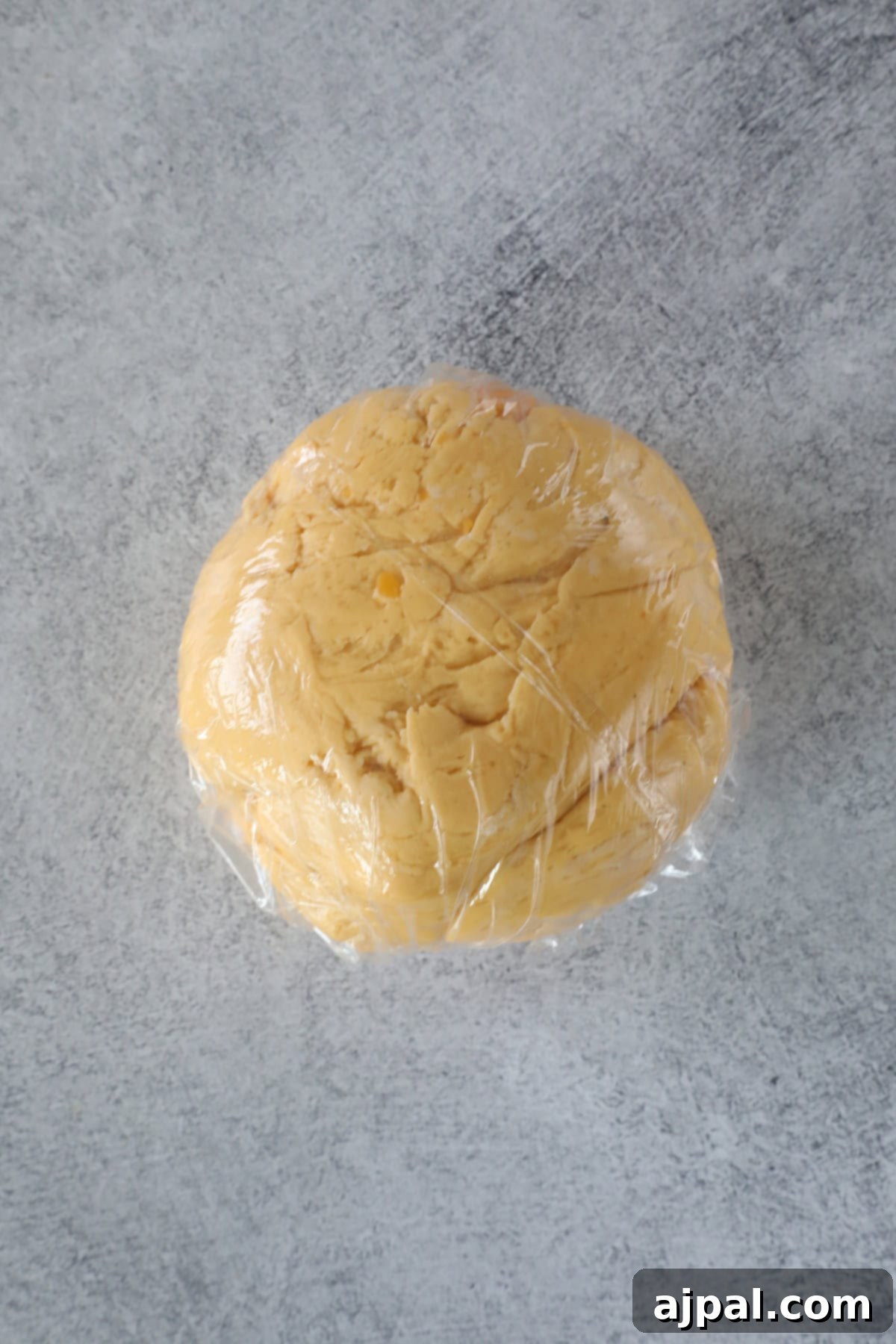 Cheesy Sourdough Discard Crisps 5 A ball of dough wrapped in clear plastic wrap rests on a gray marble surface, ready to transform into tangy sourdough crackers.