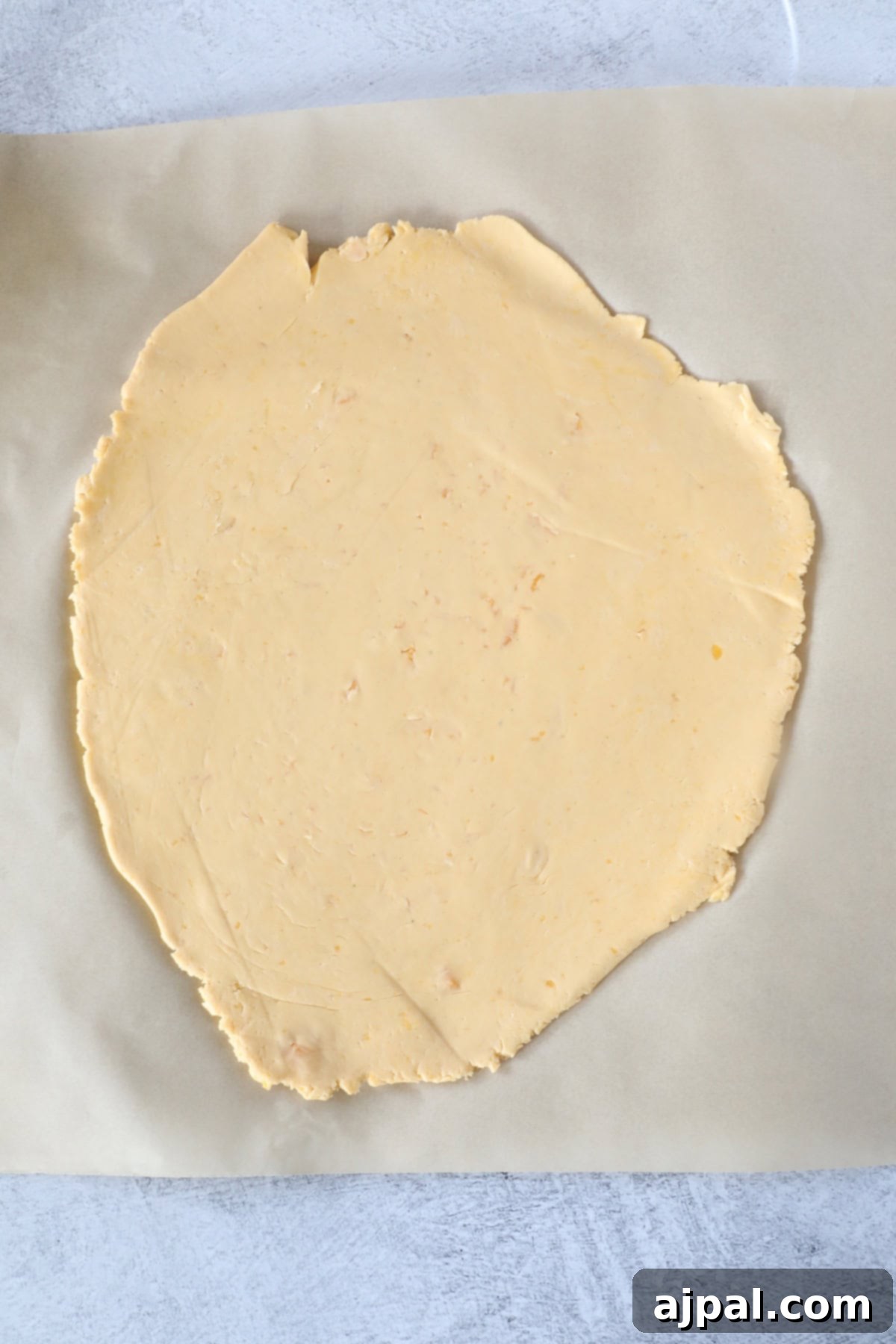 Cheesy Sourdough Discard Crisps 6 A circular sheet of dough made with sourdough discard, rolled out on parchment paper, ready for baking into delightful crackers.