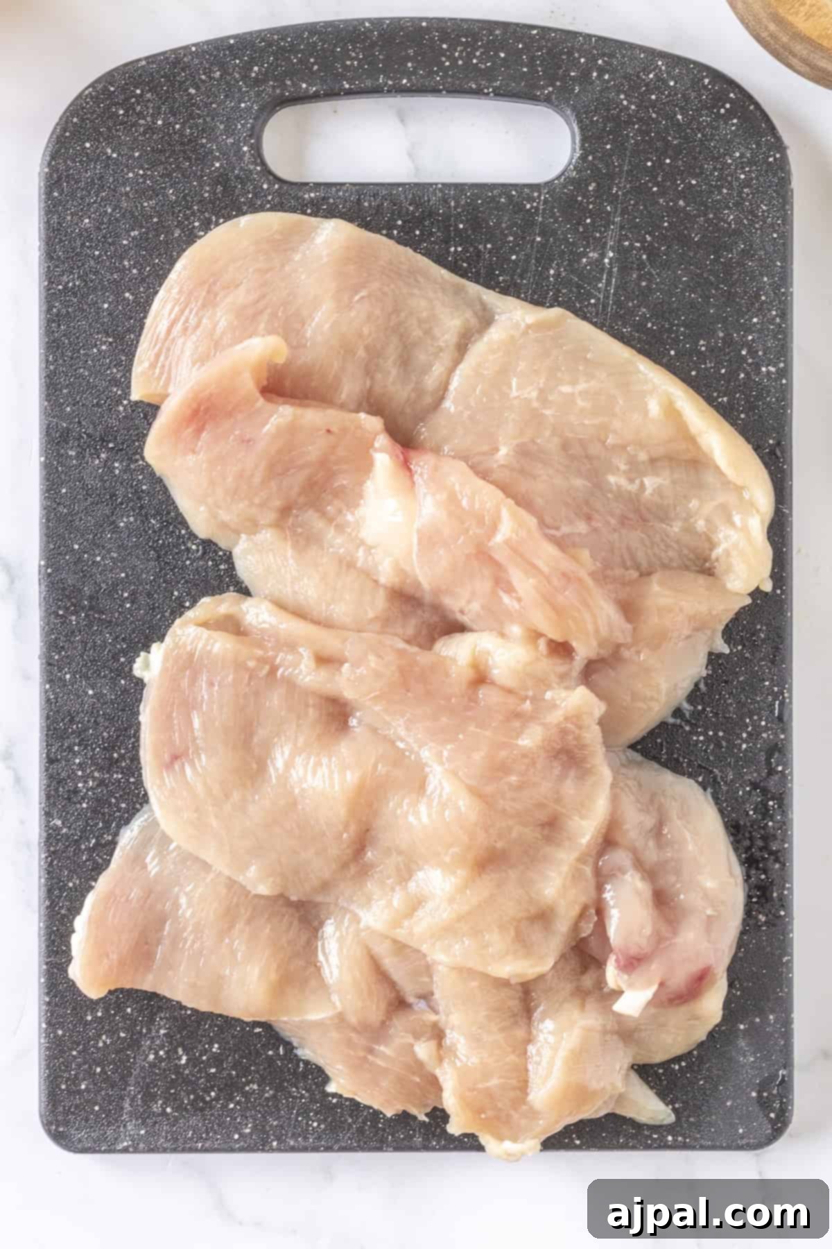 Thin chicken breasts rest on a sleek black cutting board, ready to be seasoned and savored.