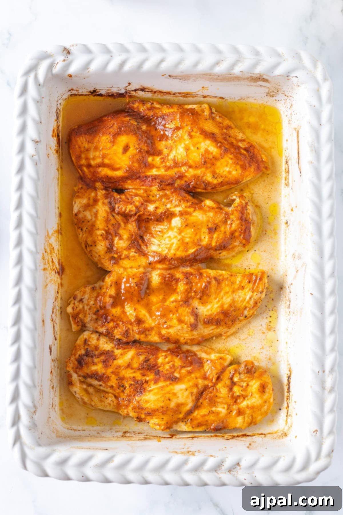 Four seasoned and thin baked chicken breasts rest perfectly in a white baking dish.