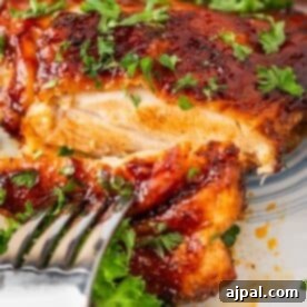 Crispy Air Fryer BBQ Chicken Thighs 14 Close-up of a fork cutting into glazed BBQ chicken, garnished with chopped parsley, on a patterned plate.