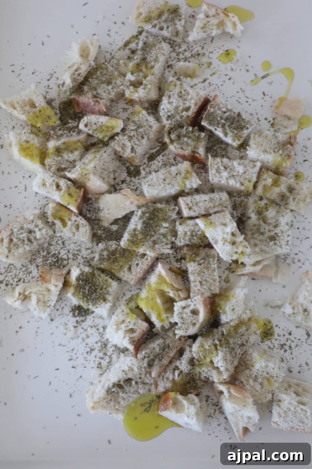 Crispy Sourdough Croutons 5 Sourdough croutons are scattered on a surface, sprinkled with herbs, grated cheese, and drizzled with olive oil.