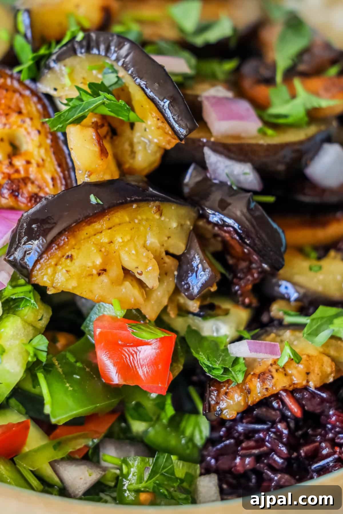 Mediterranean Vegan Sabich Bowls 2 A close-up of a mixed salad with roasted eggplant slices, diced red onion, tomatoes, chopped herbs, and mixed greens.