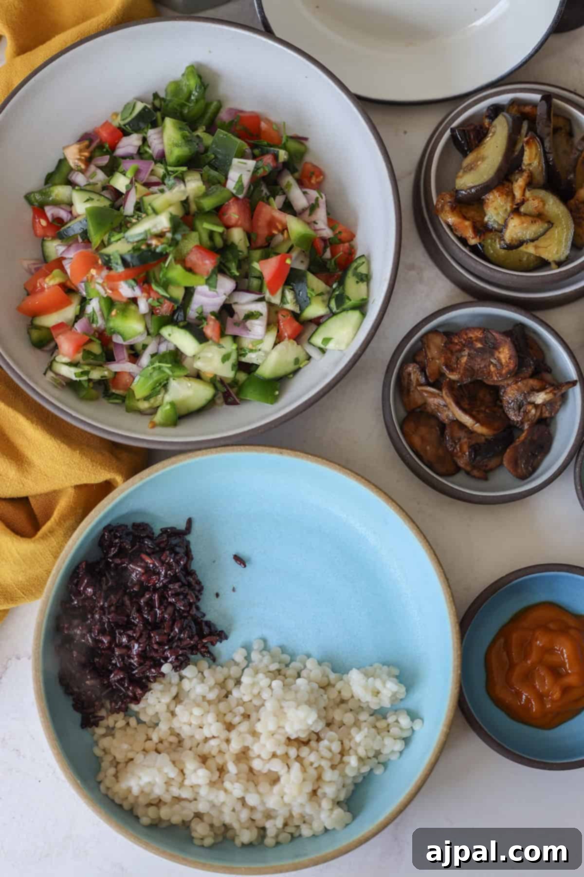 Mediterranean Vegan Sabich Bowls 11 Bowls of vibrant mixed salad, grilled vegetables, couscous, and black rice accompany a small bowl of sauce on the table, creating a picturesque vegan feast reminiscent of a sabich spread.