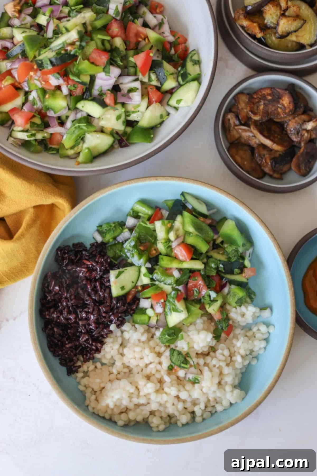 Mediterranean Vegan Sabich Bowls 12 A vibrant bowl with black rice, couscous, and fresh salad sits alongside bowls of salad, roasted eggplant, and mushrooms, reminiscent of a vegan Sabich spread on a light surface accented by a sunny yellow cloth.