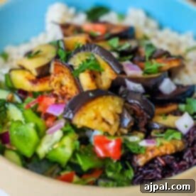 A savory sabich bowl featuring a bed of rice piled high with roasted eggplant, fresh diced vegetables, and vibrant herbs—a perfect vegan delight.