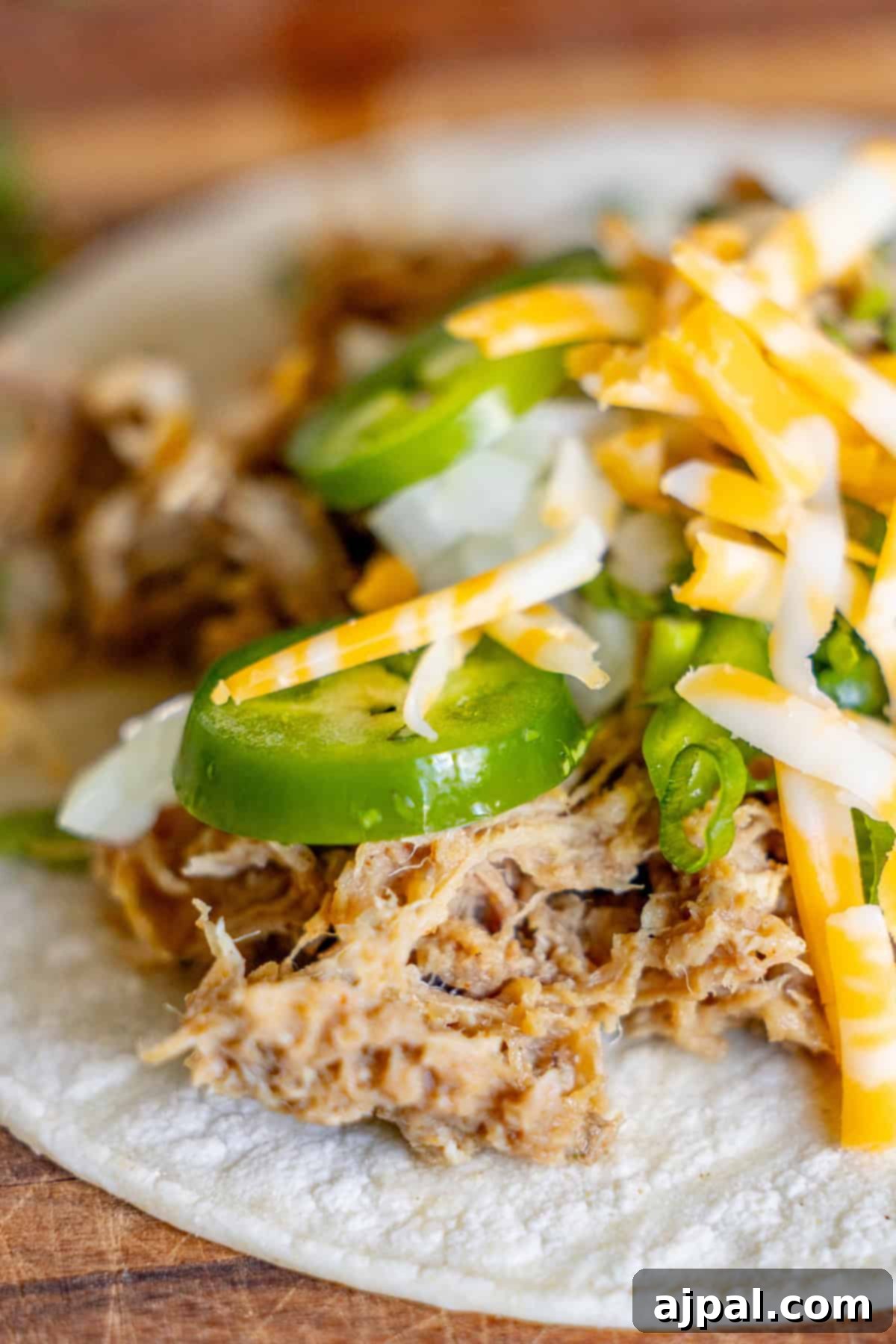 Perfectly Tender Crispy Slow Cooker Carnitas 2 A close-up of a taco generously filled with tender Slow Cooker Carnitas, vibrant sliced jalapeños, finely chopped onions, and a sprinkle of shredded cheese, all served on a soft flour tortilla.