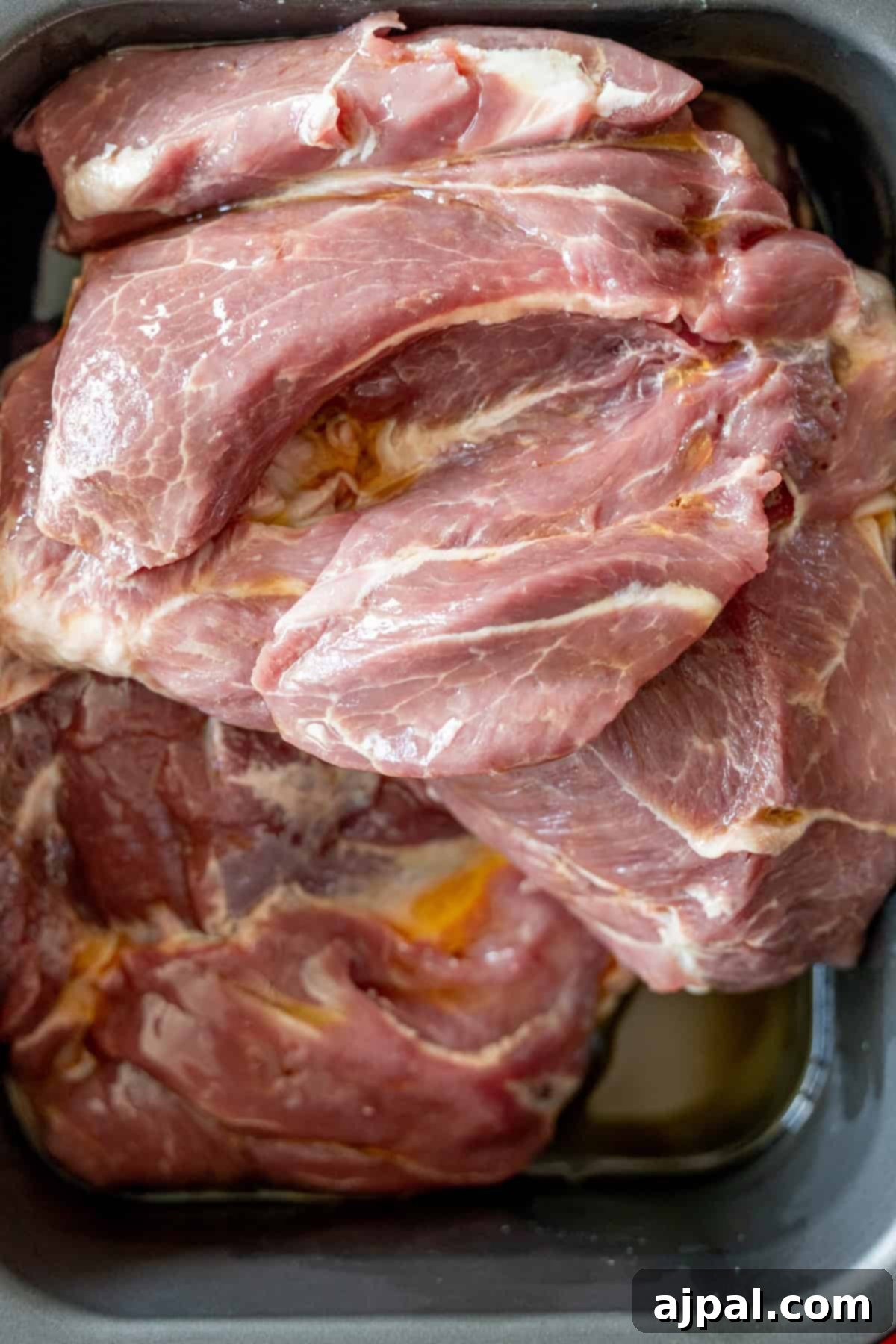 Perfectly Tender Crispy Slow Cooker Carnitas 3 Raw pieces of pork shoulder, generously coated in aromatic spices and ready to be slow-cooked, resting in a black tray with some flavorful liquid at the bottom. This sets the stage for tender Slow Cooker Carnitas.