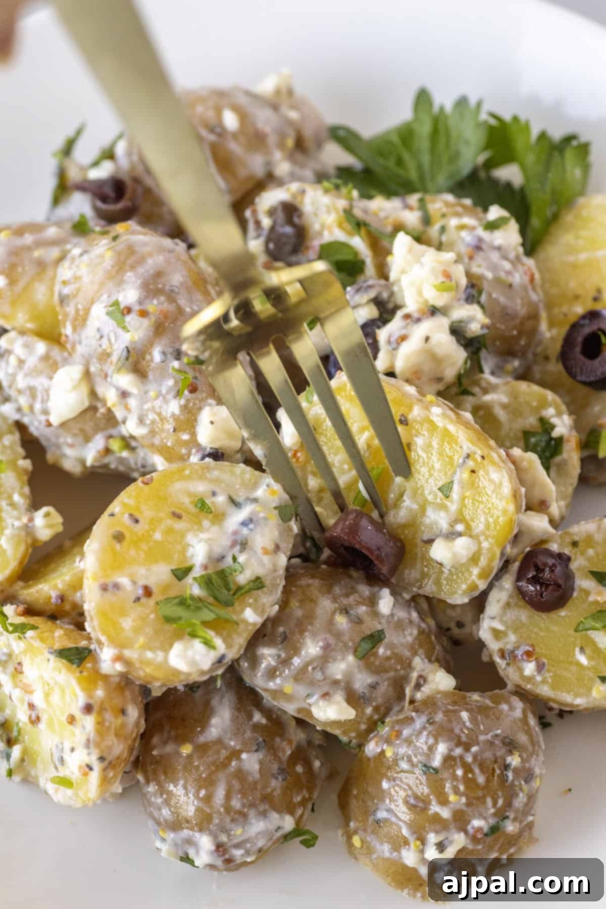 Classic Greek Potato Salad 11 A fork poised over a plate of Greek Potato Salad—sliced potatoes mixed with creamy dressing, herbs, feta cheese, and black olives.