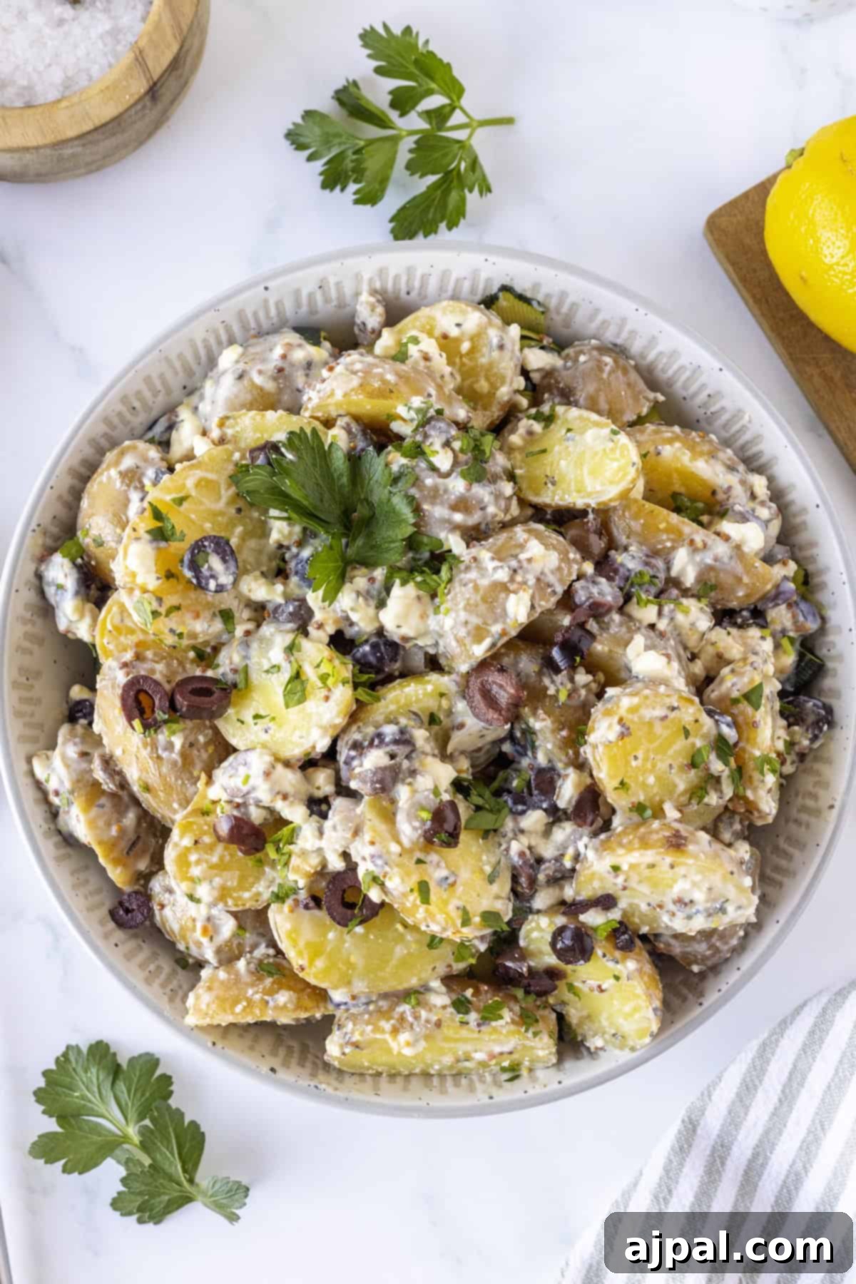 Classic Greek Potato Salad 8 A bowl of Greek Potato Salad with sliced potatoes, crumbled feta cheese, chopped parsley, and sliced black olives, garnished with fresh herbs.
