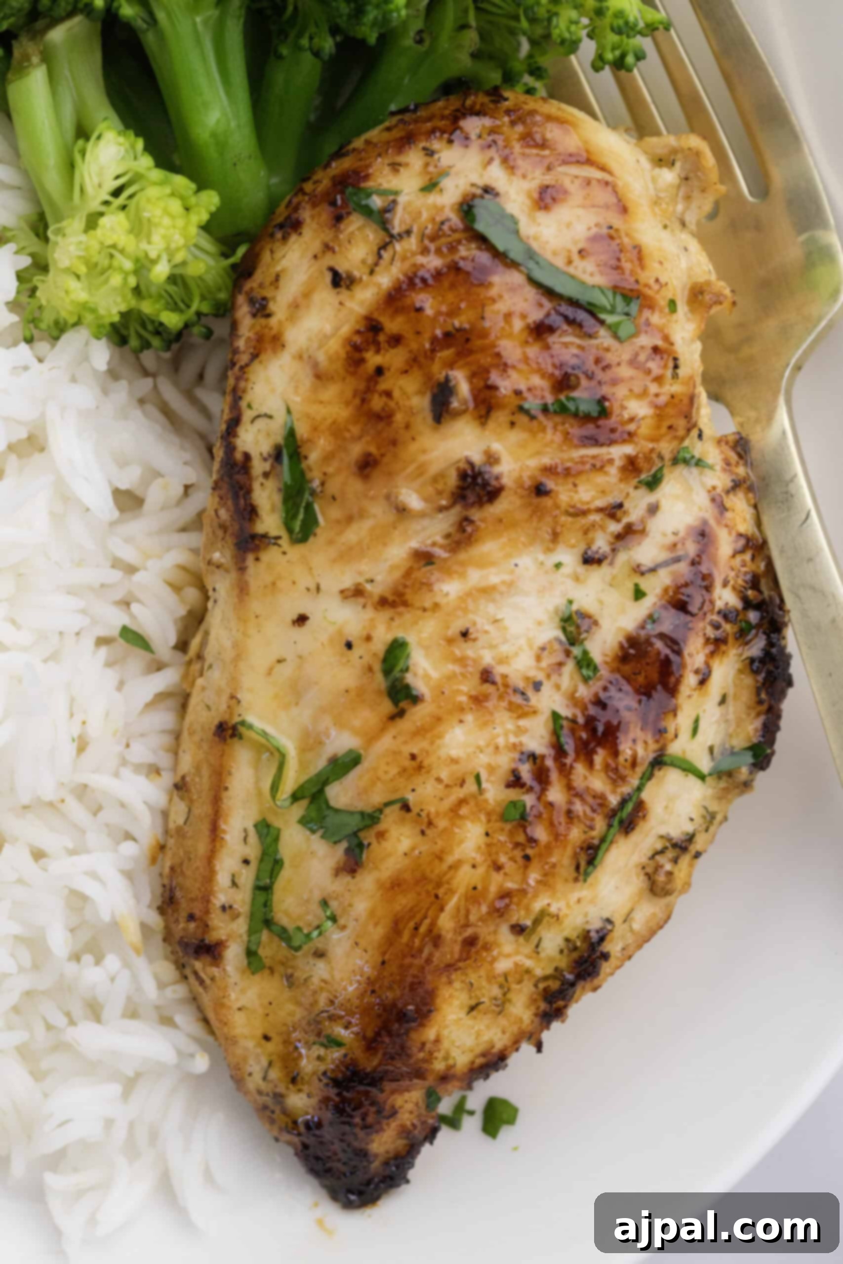 Ranch Infused Chicken Breasts 2 A delicious Ranch Chicken Breast garnished with fresh herbs, served alongside fluffy white rice and vibrant steamed broccoli on a clean white plate with a silver fork.