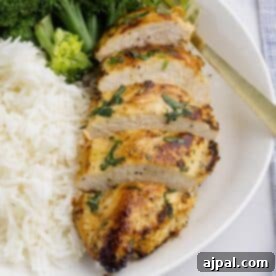 Sliced Baked Ranch Chicken breast garnished with herbs, served with white rice and steamed broccoli on a white plate.