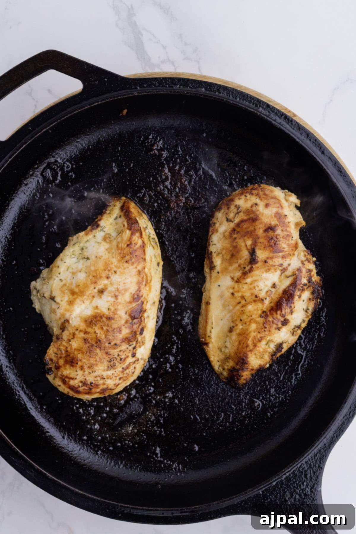 Ranch Infused Chicken Breasts 5 Two seasoned Ranch Chicken Breasts are cooked to perfection in a cast iron skillet, resting on a white marble surface—a simple yet flavorful addition to your favorite chicken recipes.