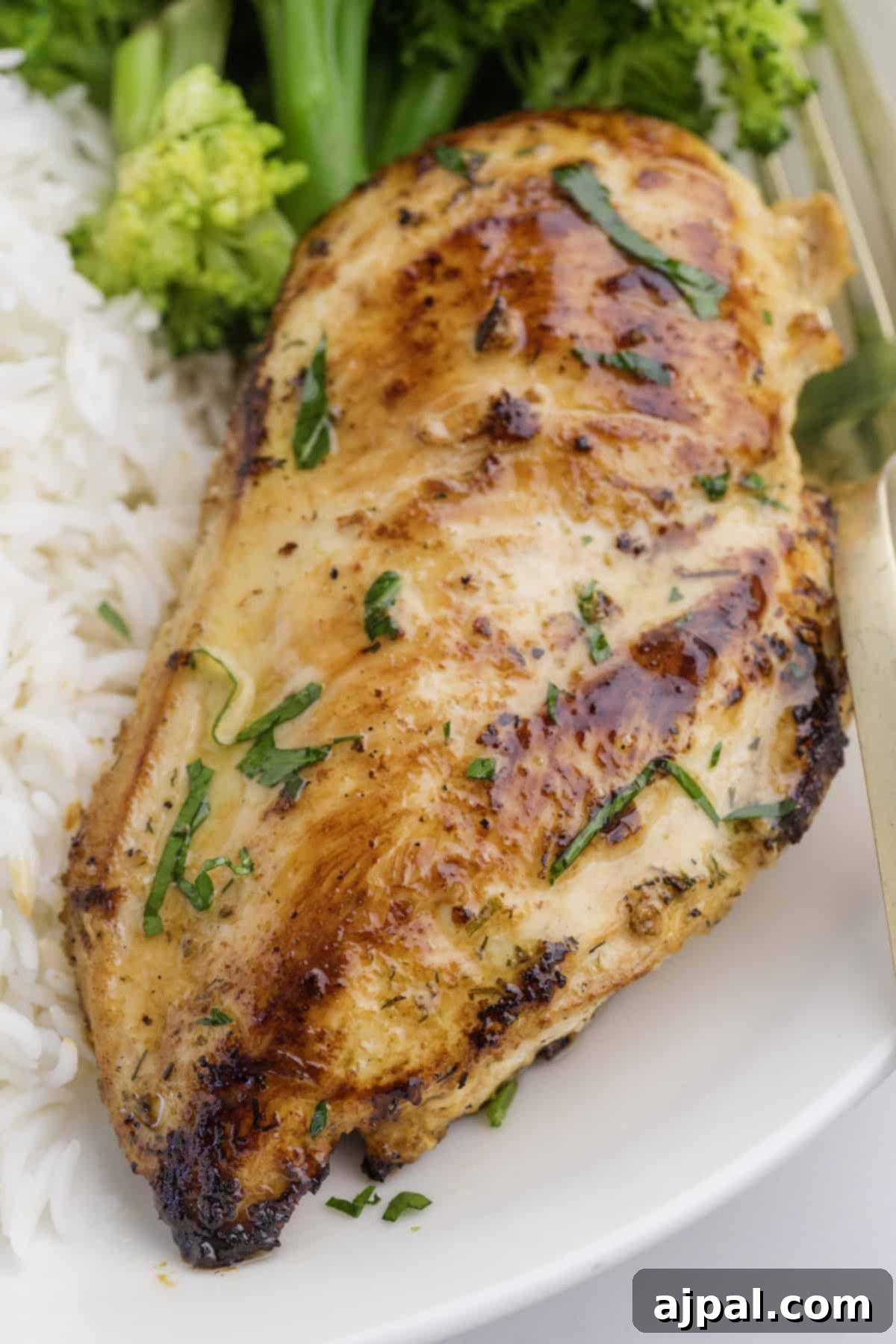 Ranch Infused Chicken Breasts 8 Ranch Chicken Breasts grilled to perfection, garnished with herbs, and served with white rice and green vegetables on a white plate.