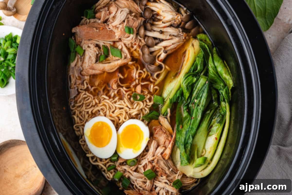 A slow cooker filled with savory chicken ramen, featuring shredded slow cooker chicken, bok choy, mushrooms, chopped green onions, ramen noodles, and two halved soft-boiled eggs in a flavorful broth.