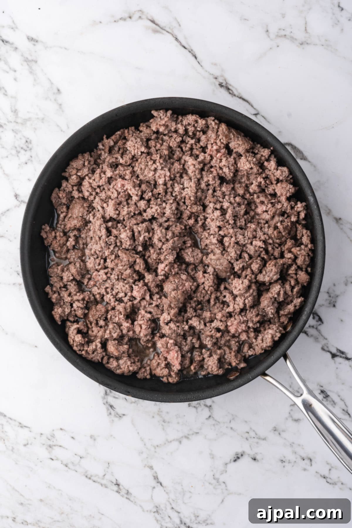 A frying pan filled with cooked ground beef for beef stroganoff sits on a white marble countertop.