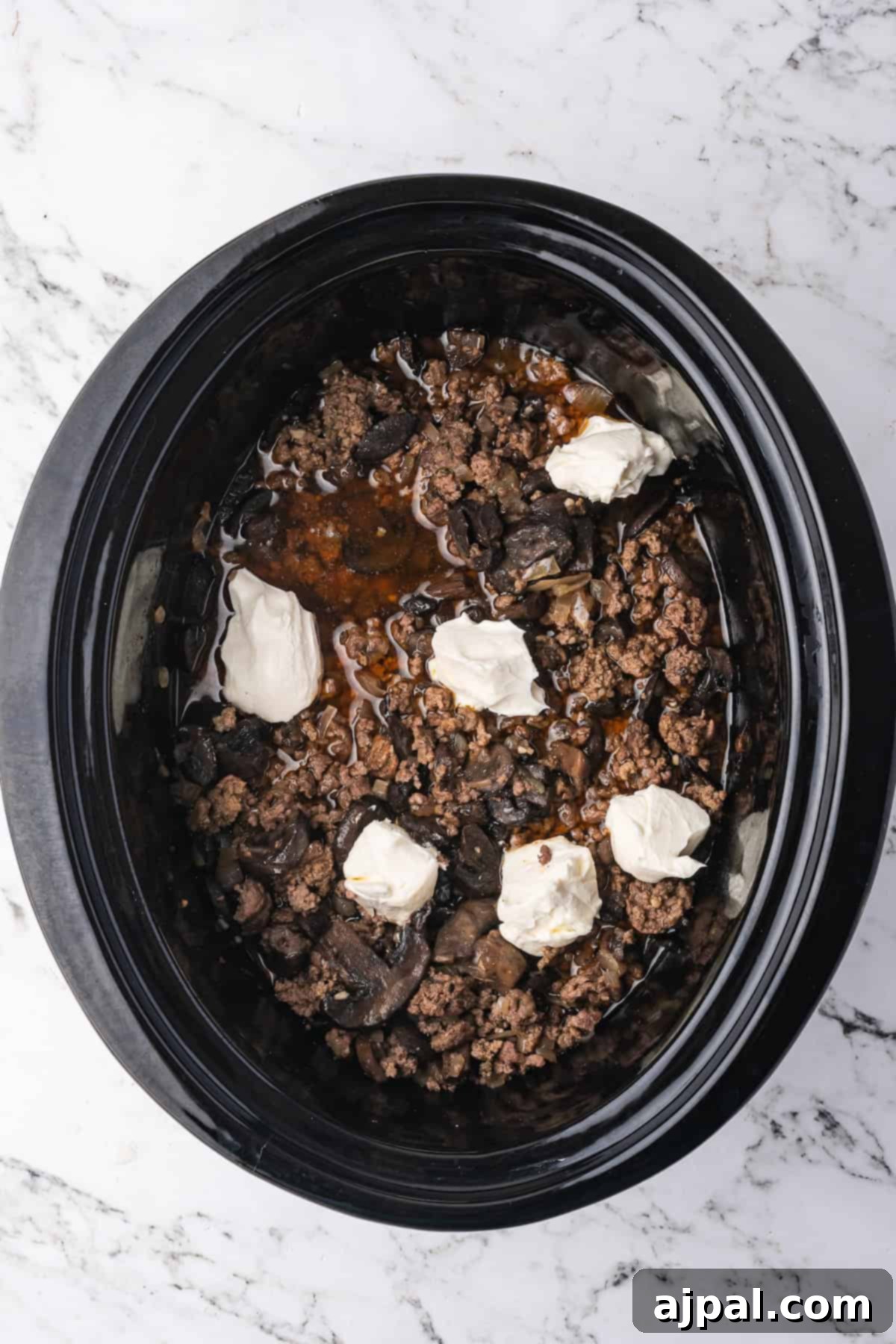 Slow Cooker Beef Stroganoff with ground beef and mushrooms, topped with dollops of sour cream, served fresh on a marble countertop.