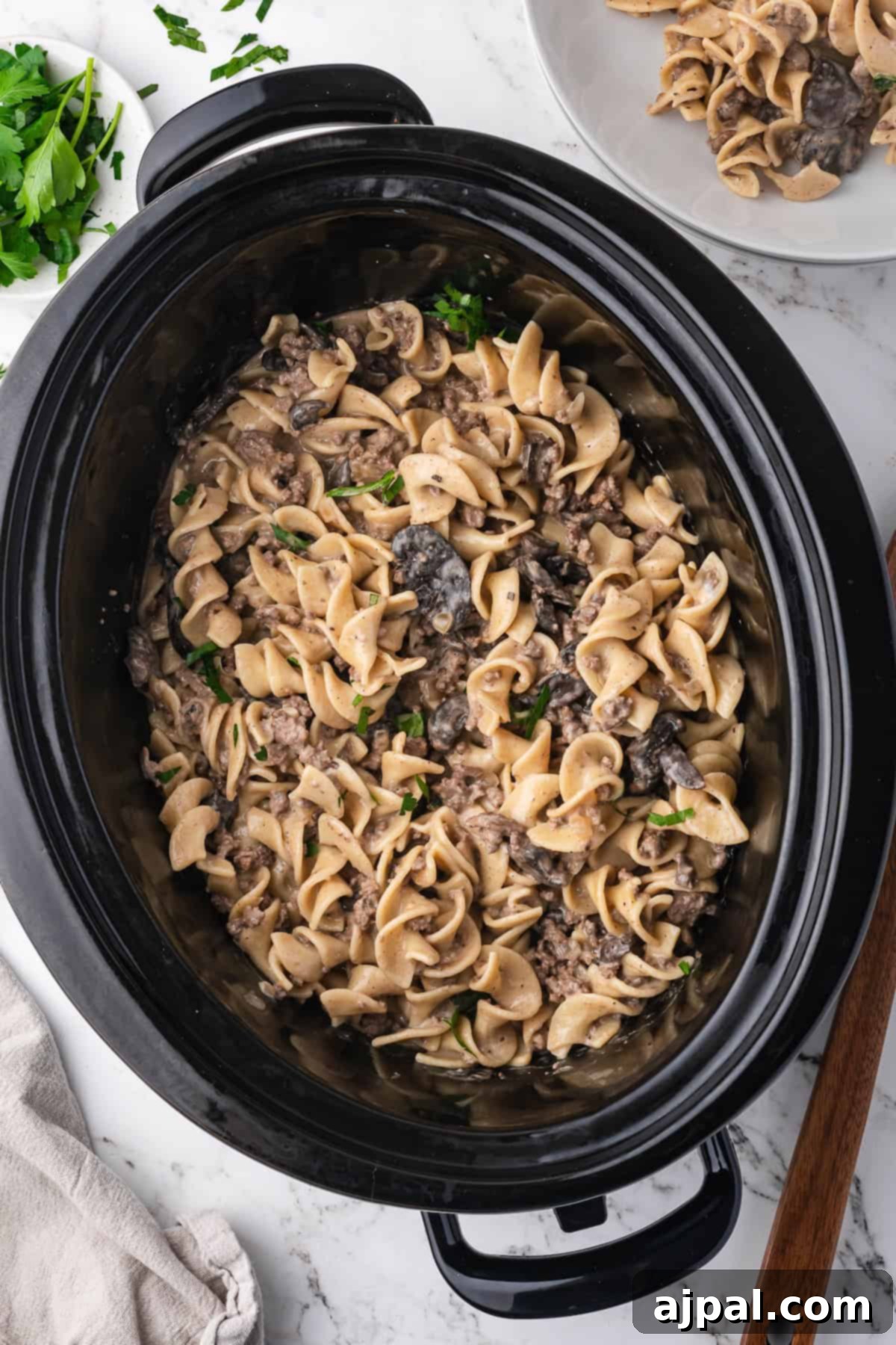 A slow cooker filled with Slow Cooker Beef Stroganoff made with tender beef, egg noodles, and mushrooms, garnished with chopped parsley.