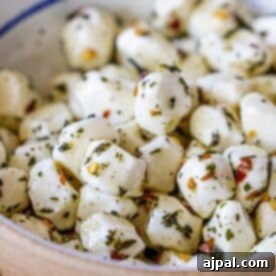A close-up of a bowl filled with perfectly marinated mozzarella balls, richly coated in aromatic herbs and savory spices. This irresistible Mozzarella Appetizer is visually stunning and promises a burst of flavor, making it ideal for any gathering or a delightful snack.
