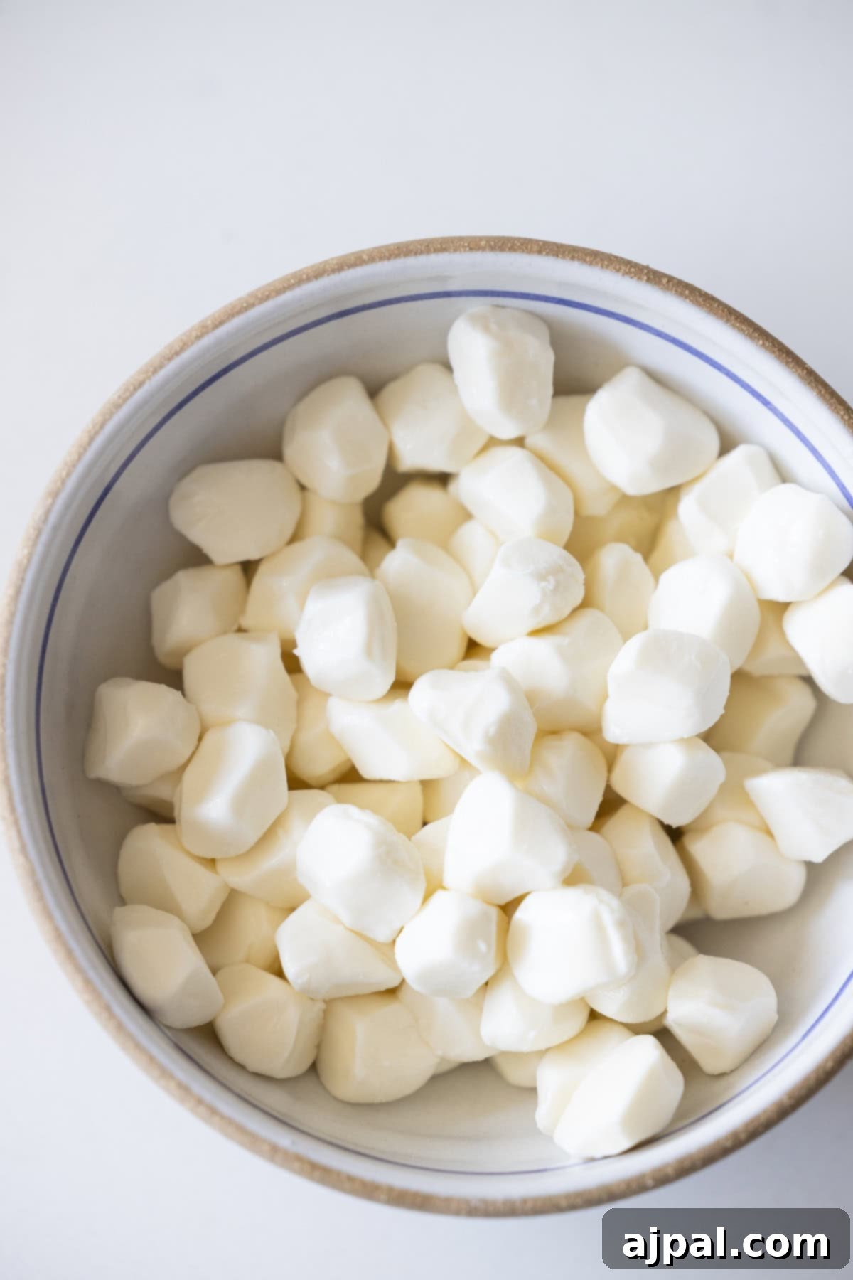 A bowl filled with small, white, perfectly dried mozzarella cheese balls, ready for marinating, on a clean white surface.