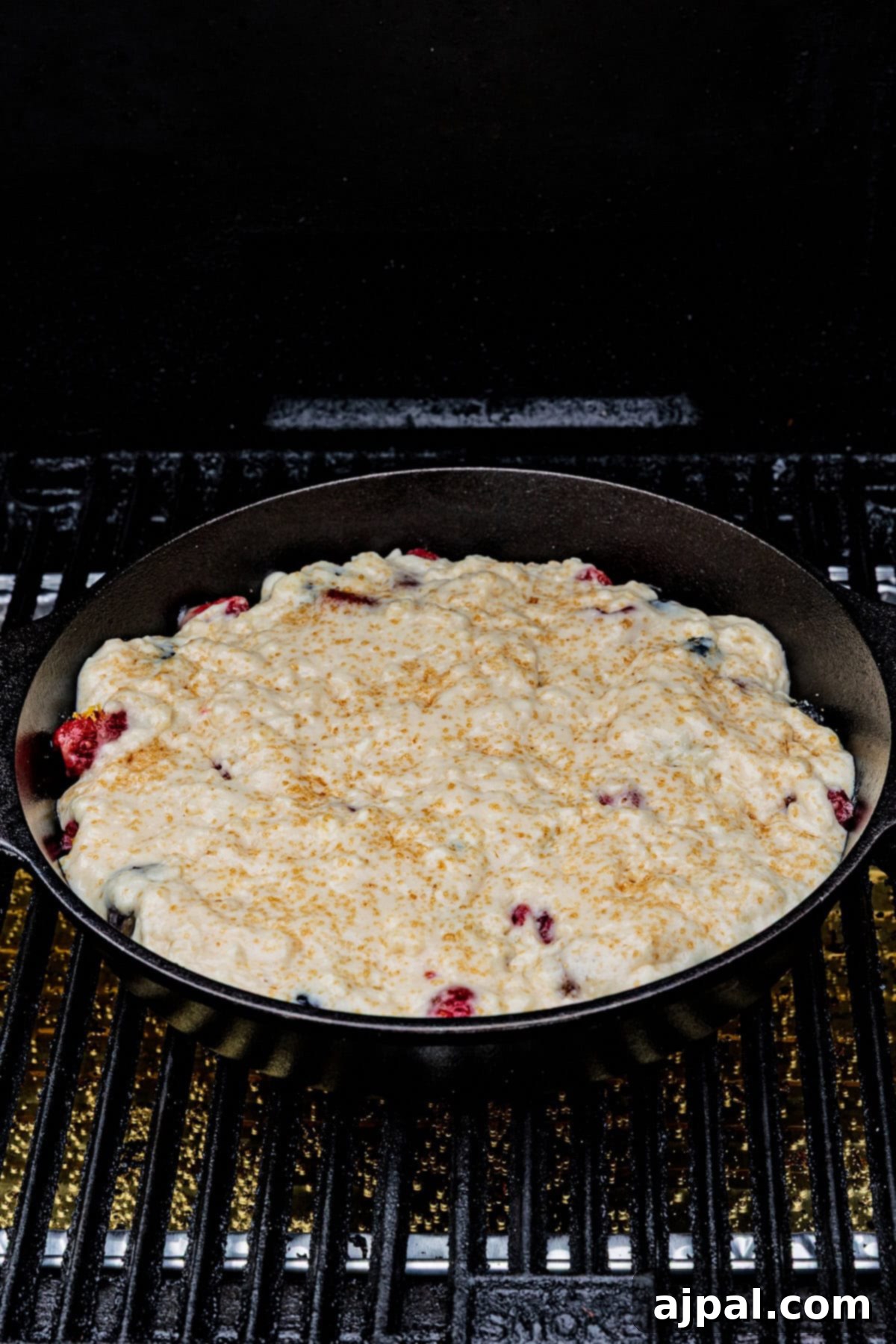 A cast iron skillet filled with unbaked Smoked Berry Cobbler batter sits on a grill, ready to be cooked.