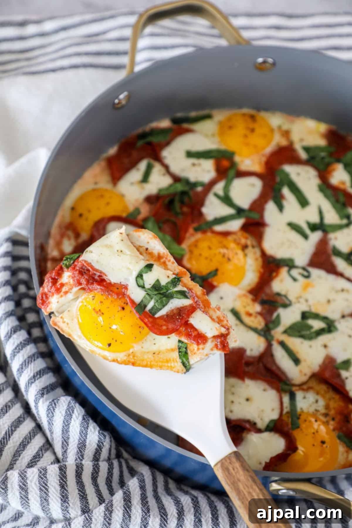 A slice of keto breakfast pizza with baked eggs, melted cheese, tomato sauce, and fresh basil is lifted from a skillet with a spatula, showcasing its gooey texture.