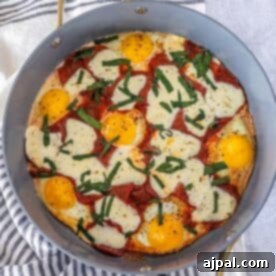 A skillet containing perfectly cooked eggs, richly melted cheese, savory pepperoni slices, and vibrant chopped basil, with a sprinkle of freshly ground pepper on top—this keto breakfast pizza is a low-carb and flavor-packed twist on a classic favorite, ready to be enjoyed.