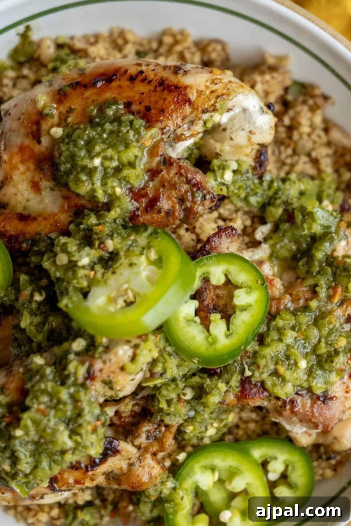 Tender grilled chicken thighs arranged over a bed of fluffy couscous, generously topped with a bright green Zhoug sauce and garnished with fresh jalapeño slices.