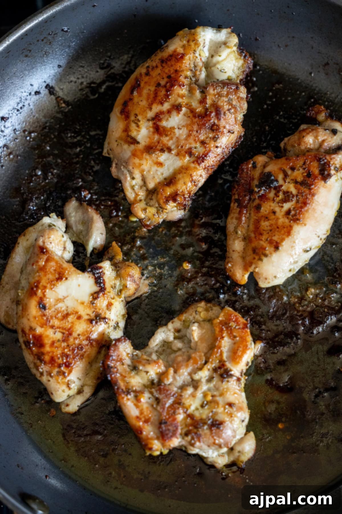 Four pieces of seasoned Zhoug chicken thighs are expertly seared in a gleaming metal skillet, showcasing a deep golden-brown and crispy surface—ideal for creating a deeply flavorful Zhoug Chicken dish.