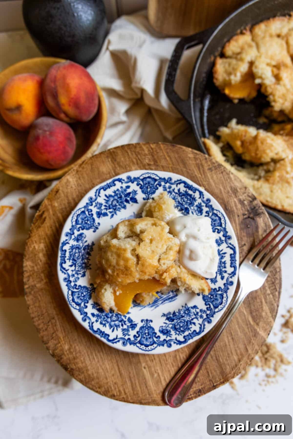 Tangy Sourdough Peach Cobbler 2 A close-up of a rustic sourdough peach cobbler with a golden-brown crust, fresh peaches peeking through, and a scoop of melting vanilla ice cream on top.