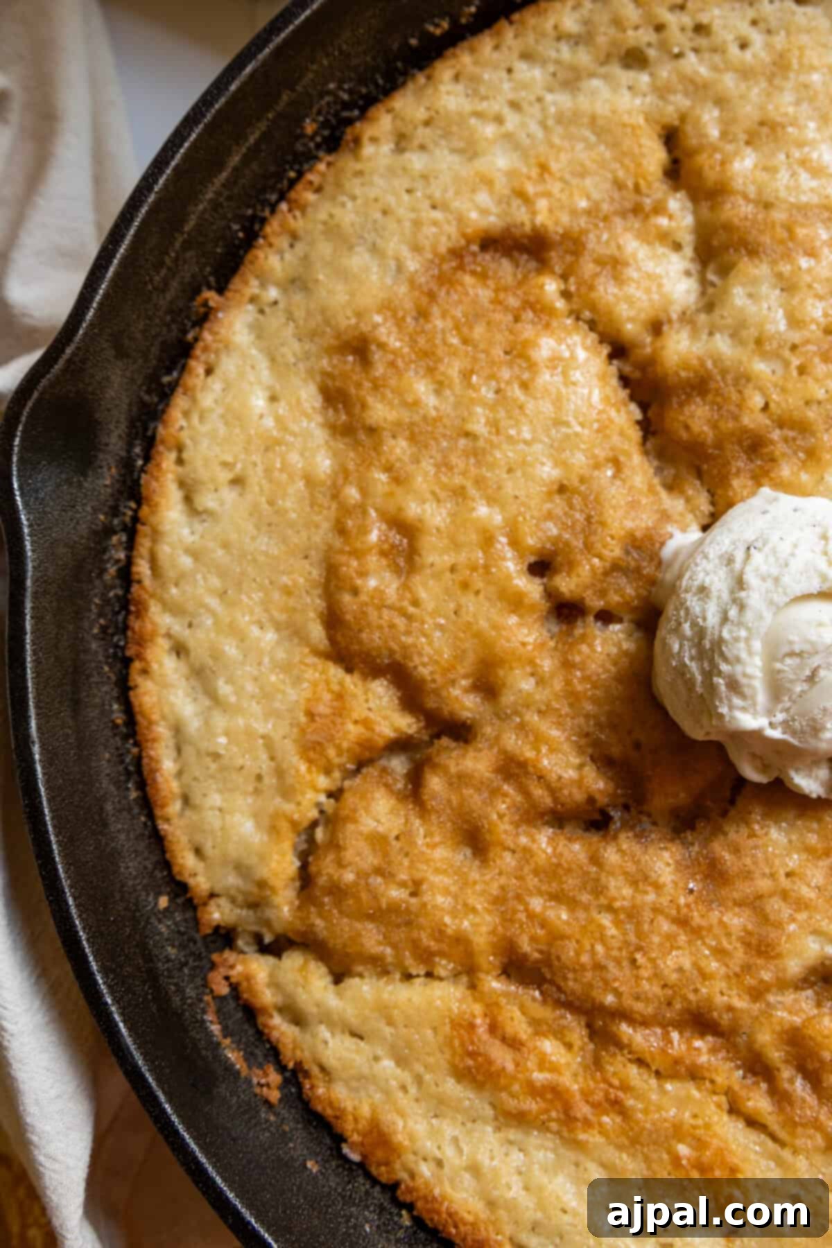 Tangy Sourdough Peach Cobbler 4 A close-up of golden-brown skillet sourdough peach cobbler, topped with a generous scoop of creamy vanilla ice cream, melting into the warm fruit.
