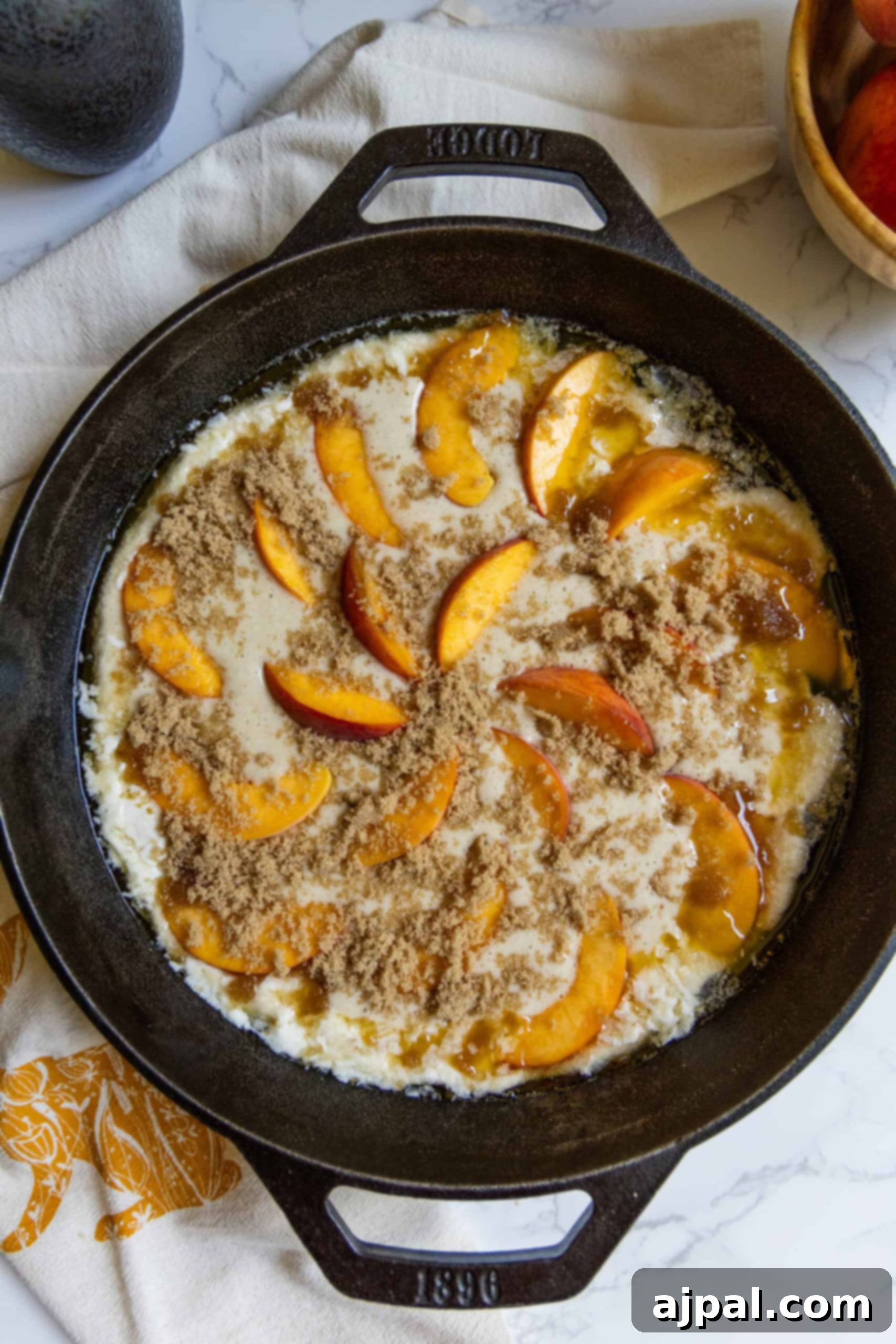 Tangy Sourdough Peach Cobbler 9 Sourdough cobbler batter poured over melted butter in a cast iron skillet, with sliced peaches and brown sugar ready to be added on top, capturing a key baking step.