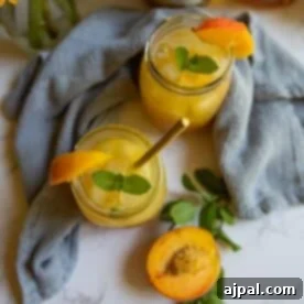 Two mason jars of bourbon peach smash cocktail with ice, garnished with mint and peach slices, placed on a light cloth, with a halved peach and mint sprigs nearby.