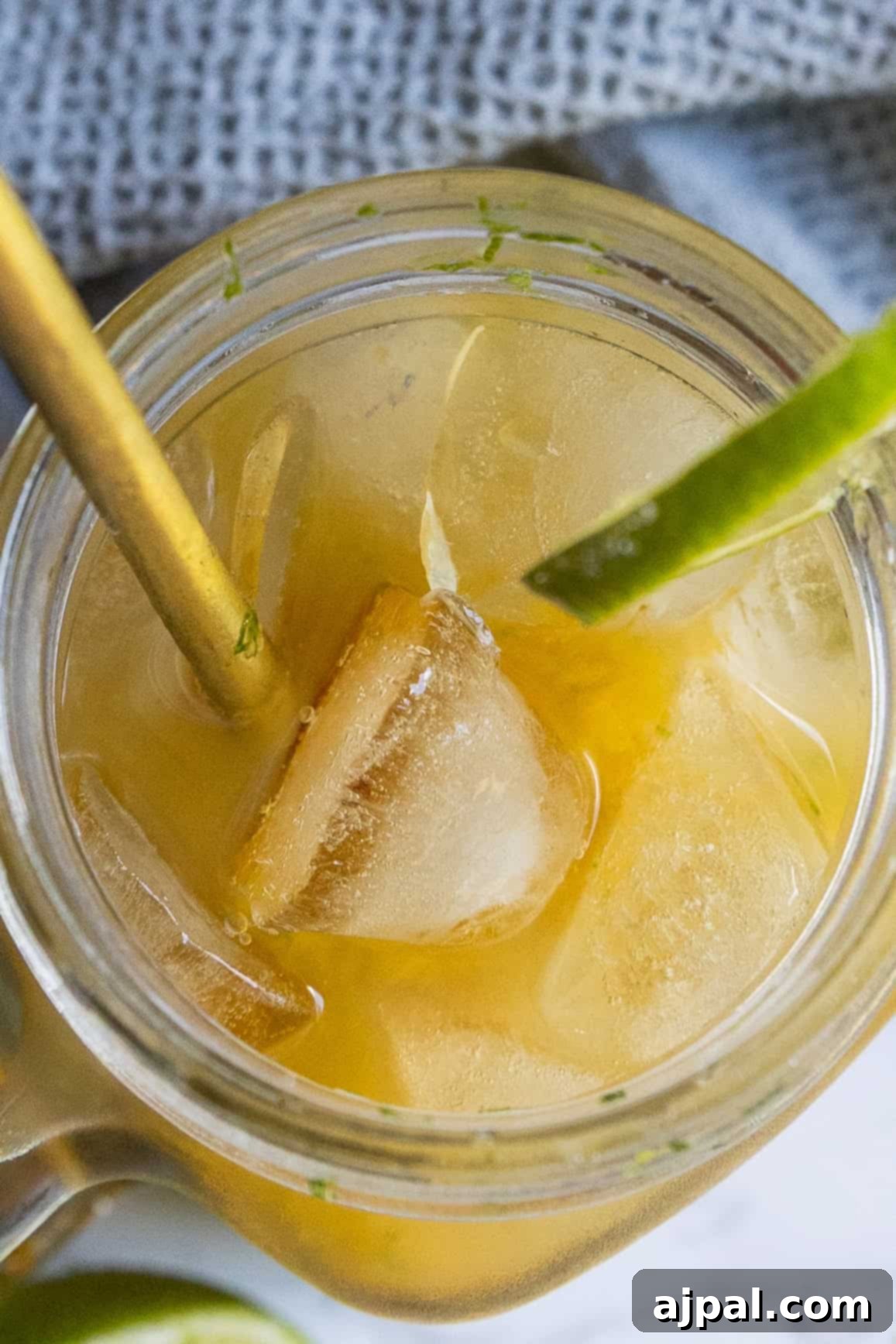A close-up top view of a peach La Croix mocktail—an iced yellow drink in a glass jar, garnished with a lime wedge and served with a metal straw.